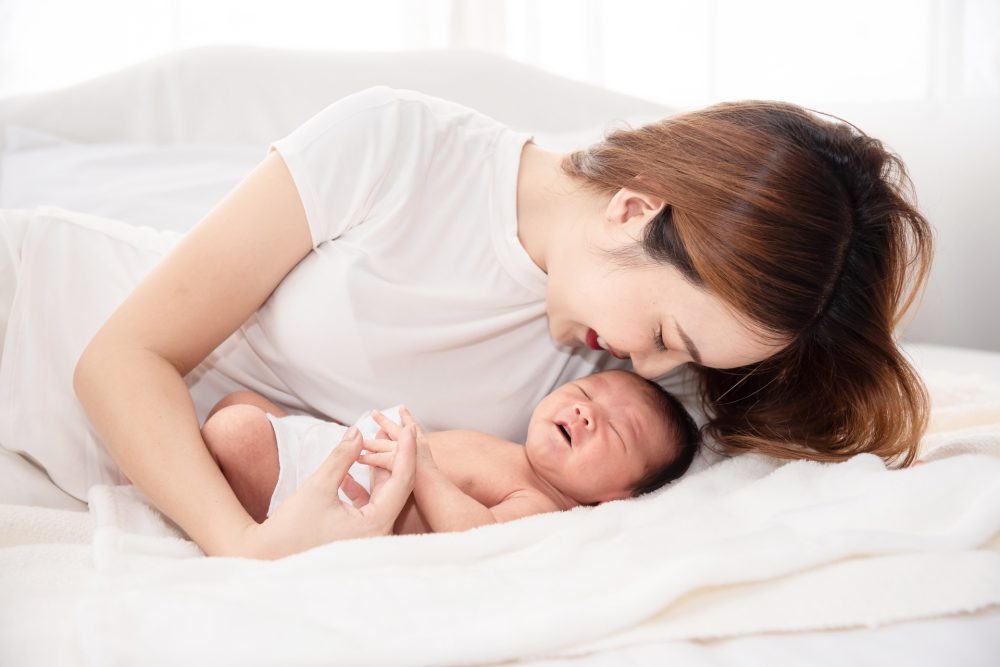 Asian loving mom carying of her newborn baby at home. Happy mum holding sleeping infant child on hands. Mother hugging her little one months old son.